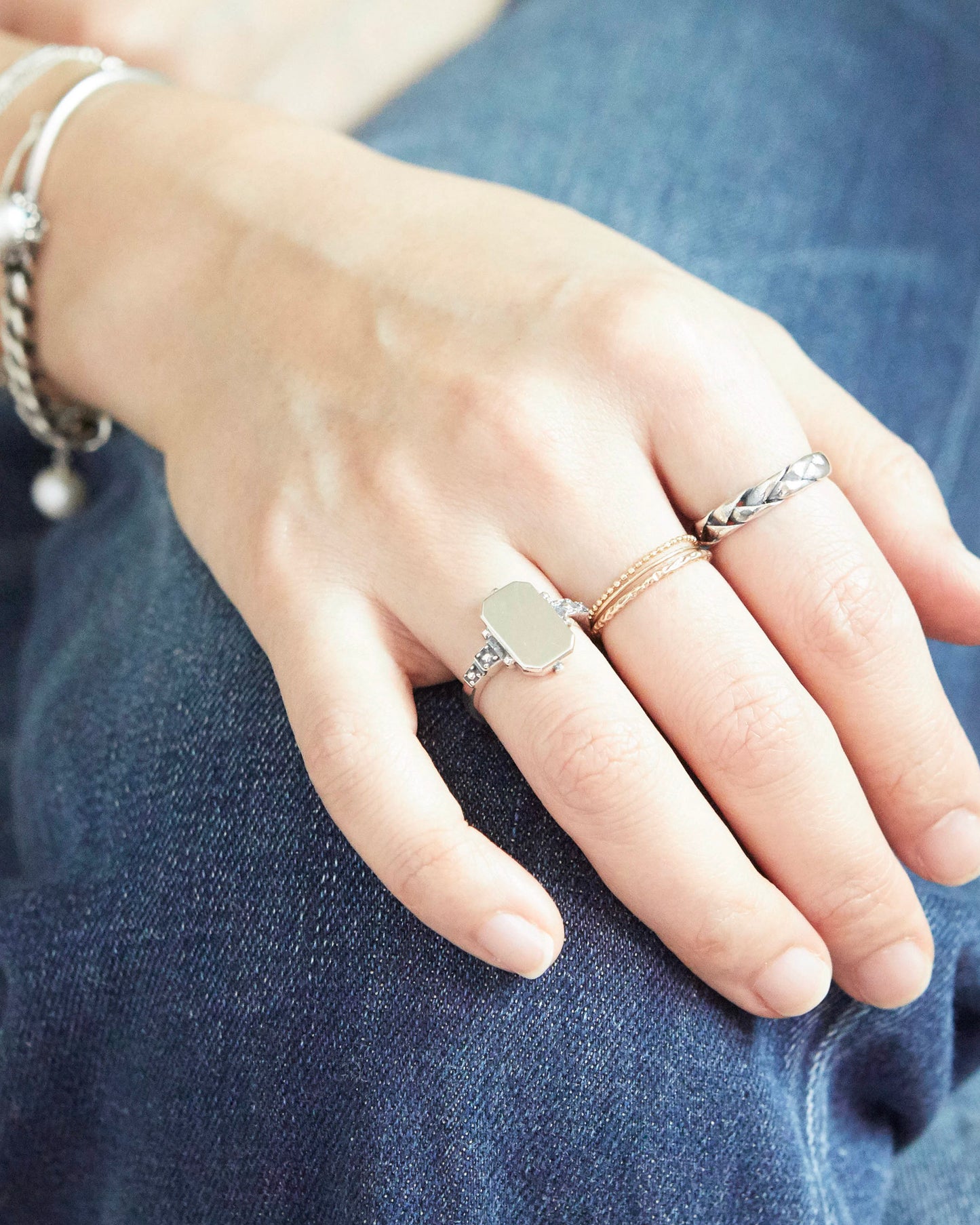 Close-up of a hand wearing multiple rings on a denim background