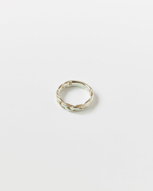 Close-up of a silver braided ring resting on a white background, showcasing its twisted woven design