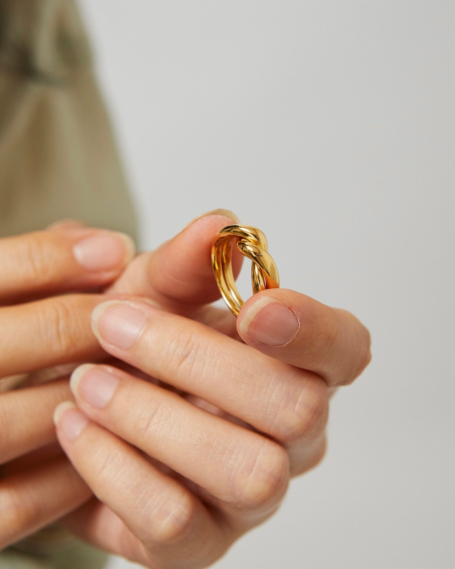 Gold ring held between fingers against a neutral background
