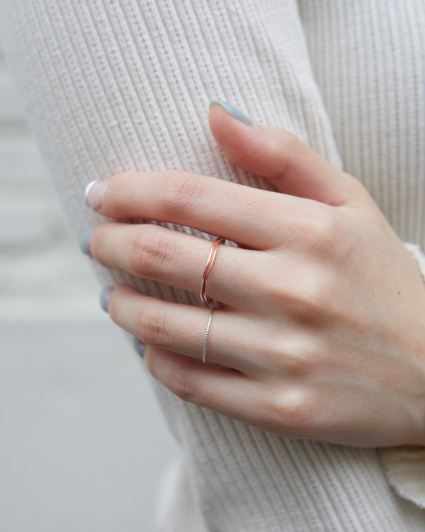 A shiny silver ring worn alongside a sculptural open ring and a thin orange band on the hand.
