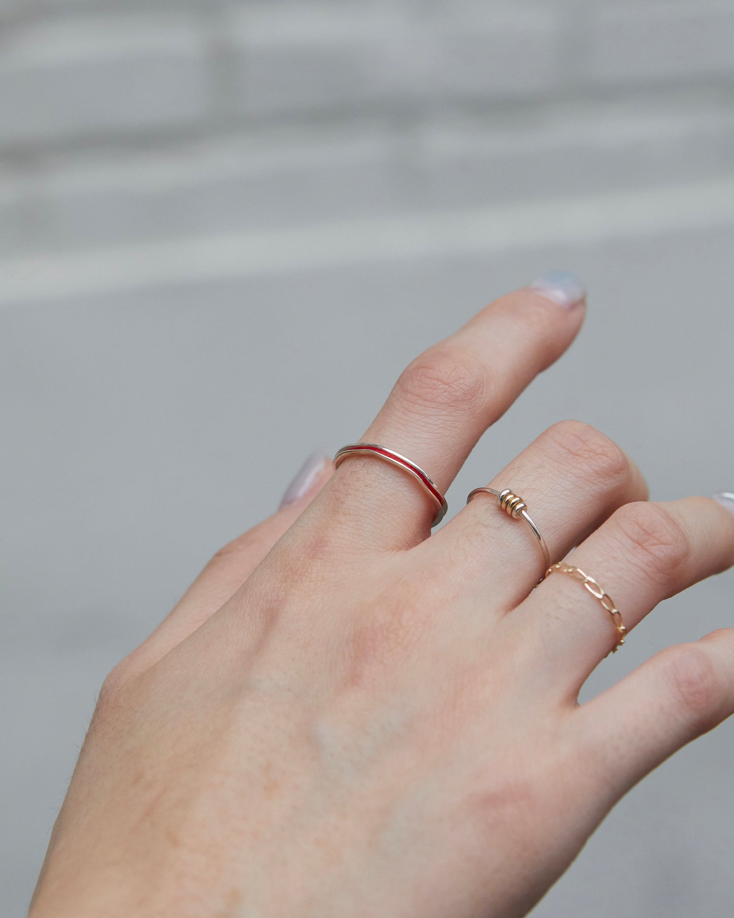 Simple silver red ring with a bold wave contour, worn solo on the middle finger.