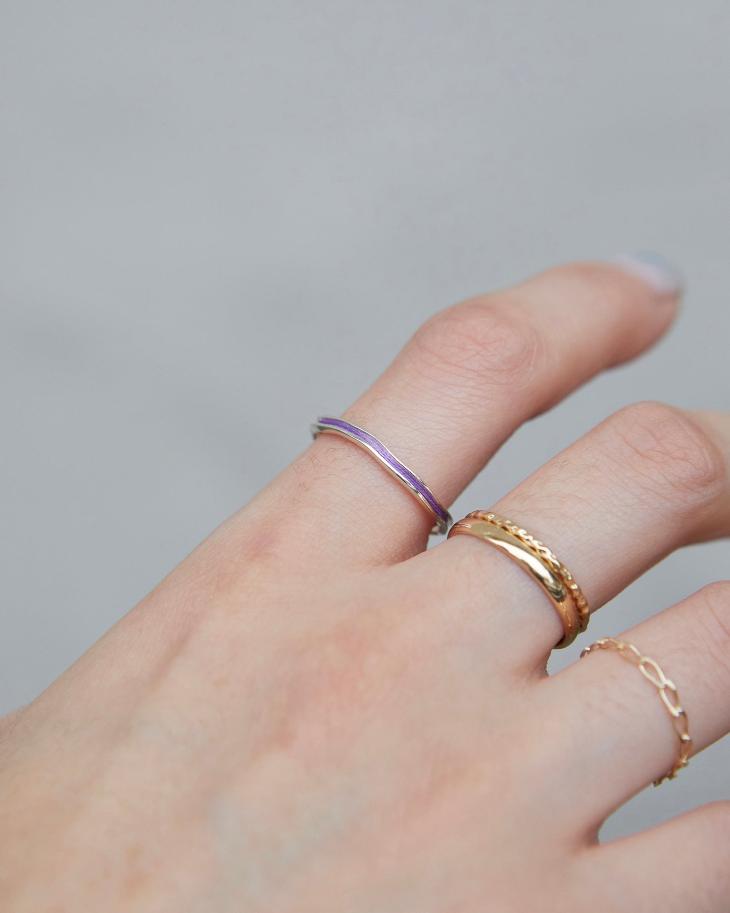 Silver ring with subtle violet worn on the ring finger, paired with delicate gold and chain rings.